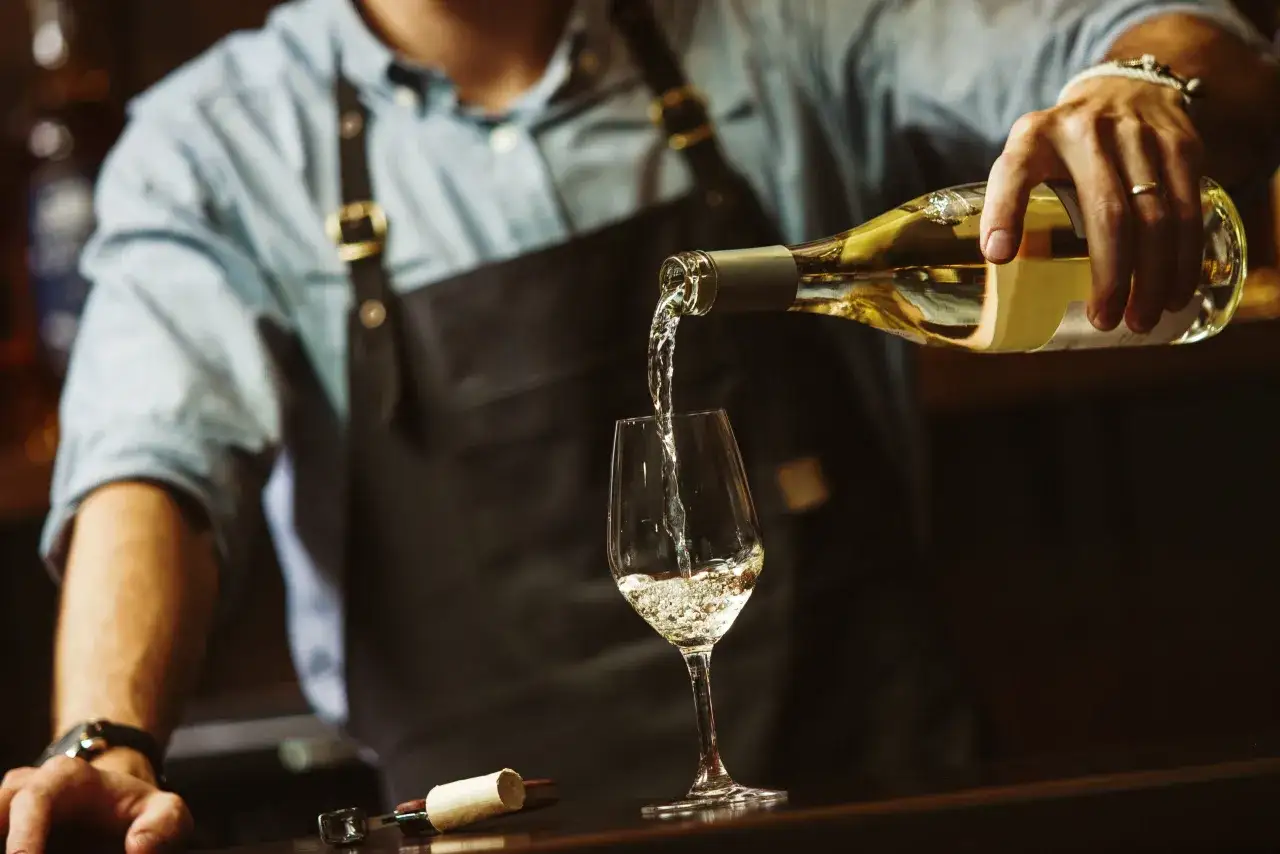 Un sommelier versa un vino pugliese bianco in un calice, creando un'atmosfera di degustazione raffinata.