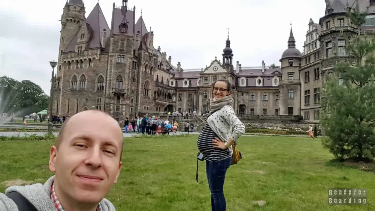 Szukacie pomysłu, gdzie na wakacje w ciąży? Para przed zamkiem, ona z brzuszkiem, cieszą się zwiedzaniem.
