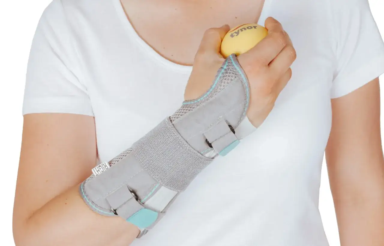 Dłoń w ortezie ćwiczy z piłeczką, co może być etapem rehabilitacji po zdjęciu gipsu. Pytanie: po jakim czasie można zmienić gips na ortezę?