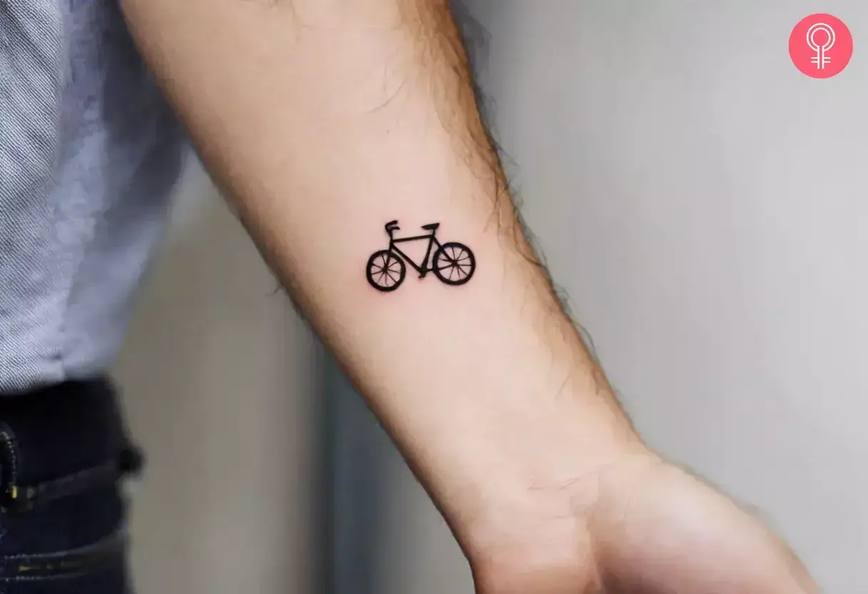 Minimalistyczny tatuaż rower na przedramieniu. Symbol wolności i podr&oacute;ży.