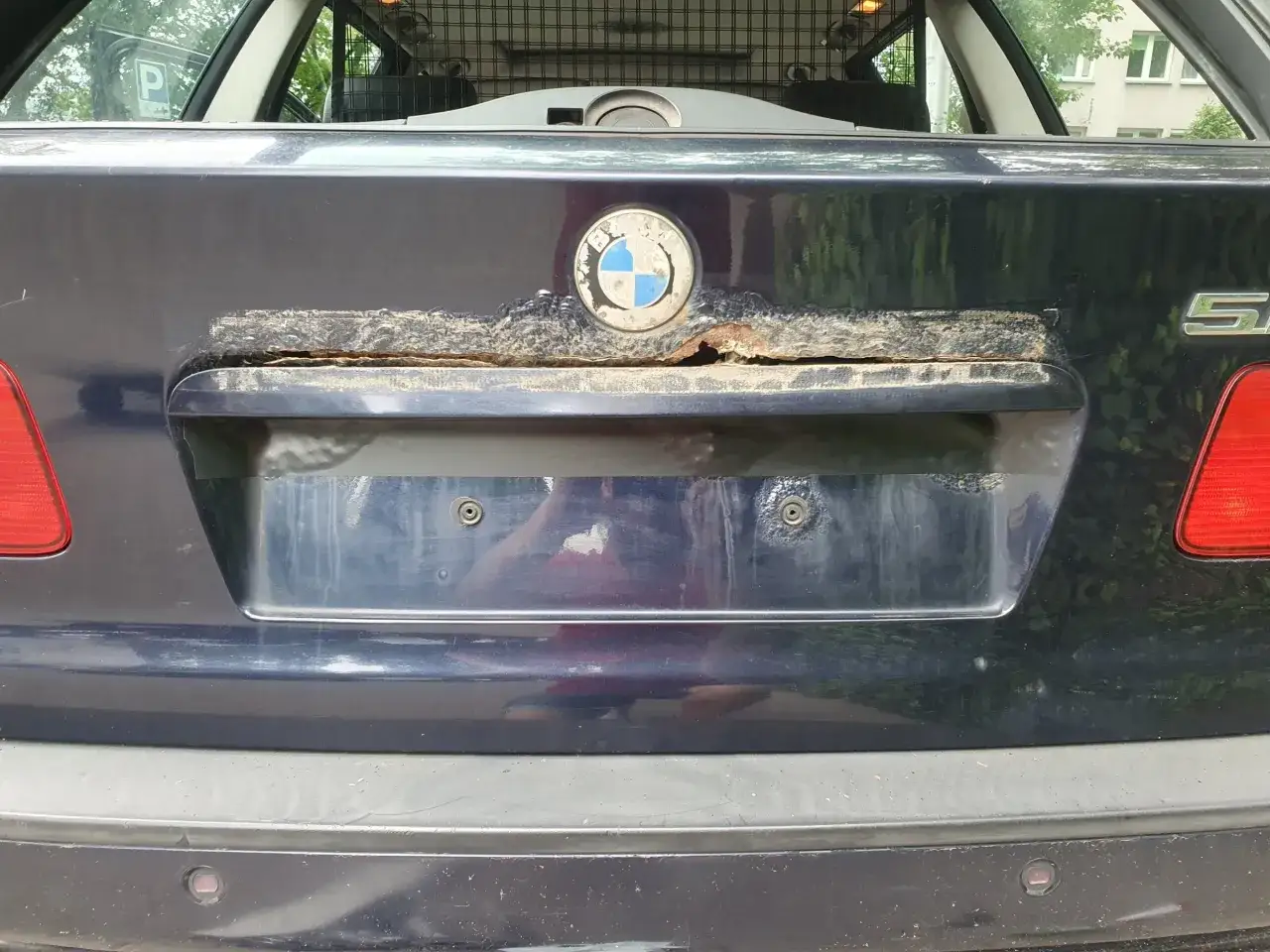 Rdza i uszkodzenia pod tablicą rejestracyjną BMW wskazują na przyczyny opadania zderzaka pod ciężarem tablicy rejestracyjnej.