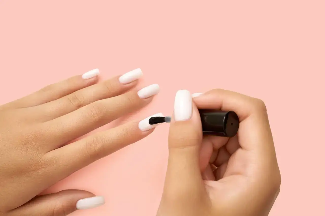 Mano che si applica smalto bianco, mostrando come si fanno le unghie perfette per un look elegante.