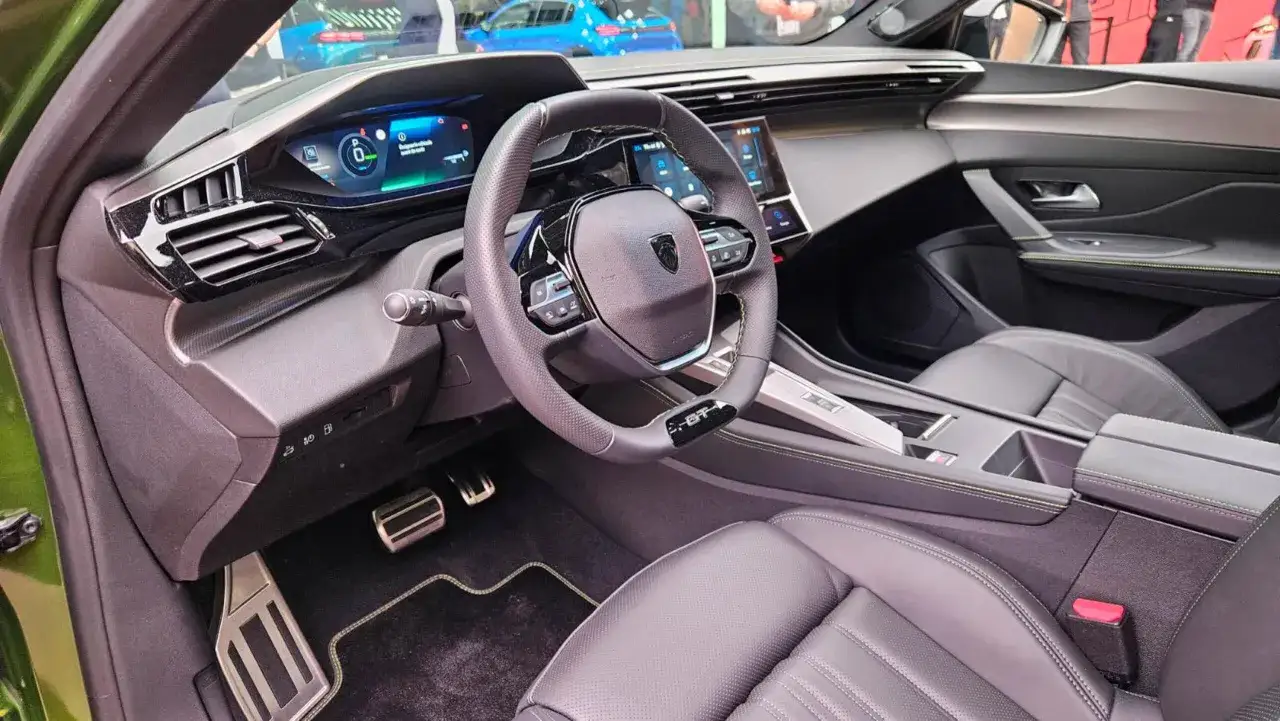 Wnętrze zielonego Peugeot 408 Hybrid: cyfrowy kokpit, skórzana kierownica i fotele, metalowe pedały.