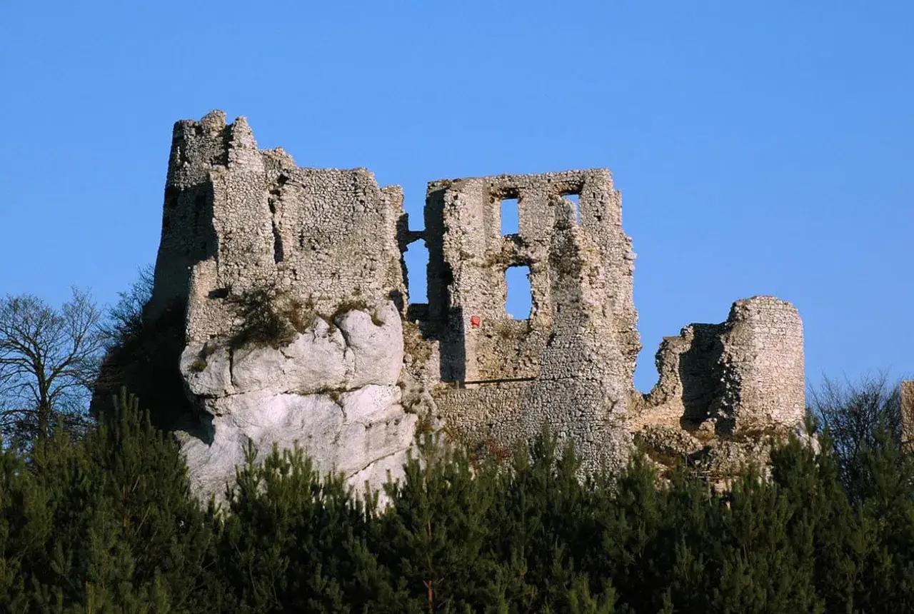 Ruiny zamku Bobolice, majestatycznie wznoszące się na skale, otoczone zielenią drzew, pod błękitnym niebem.