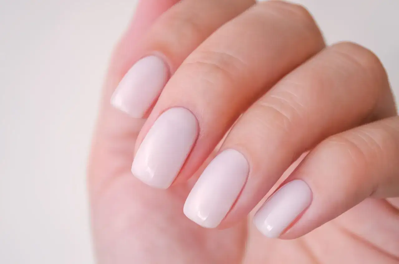 Main d'une femme avec un ongle blanc laiteux, d'une douceur subtile et d'une finition impeccable.
