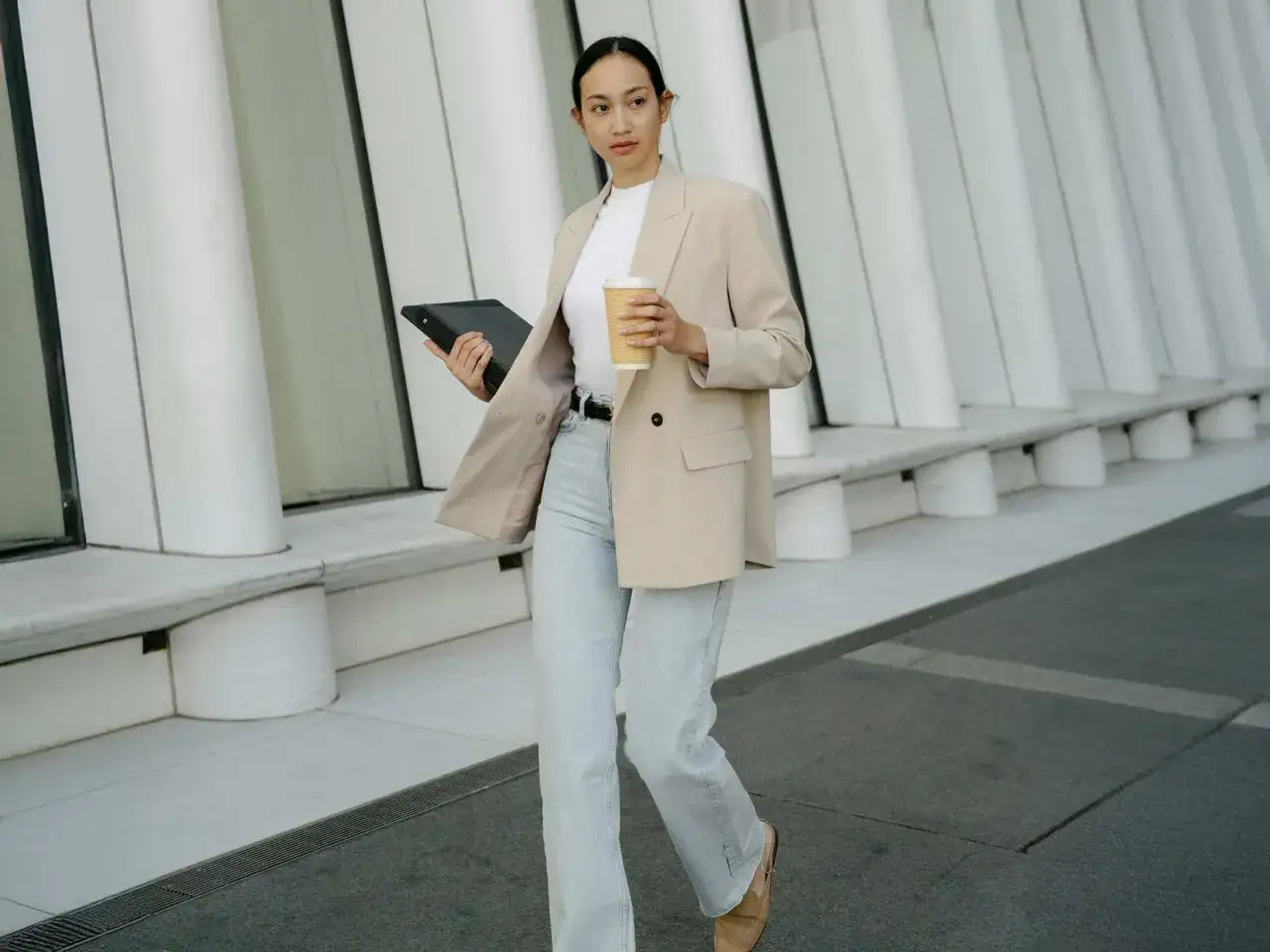 Frau im smart casual Look mit beigem Blazer, Jeans und Tablet.