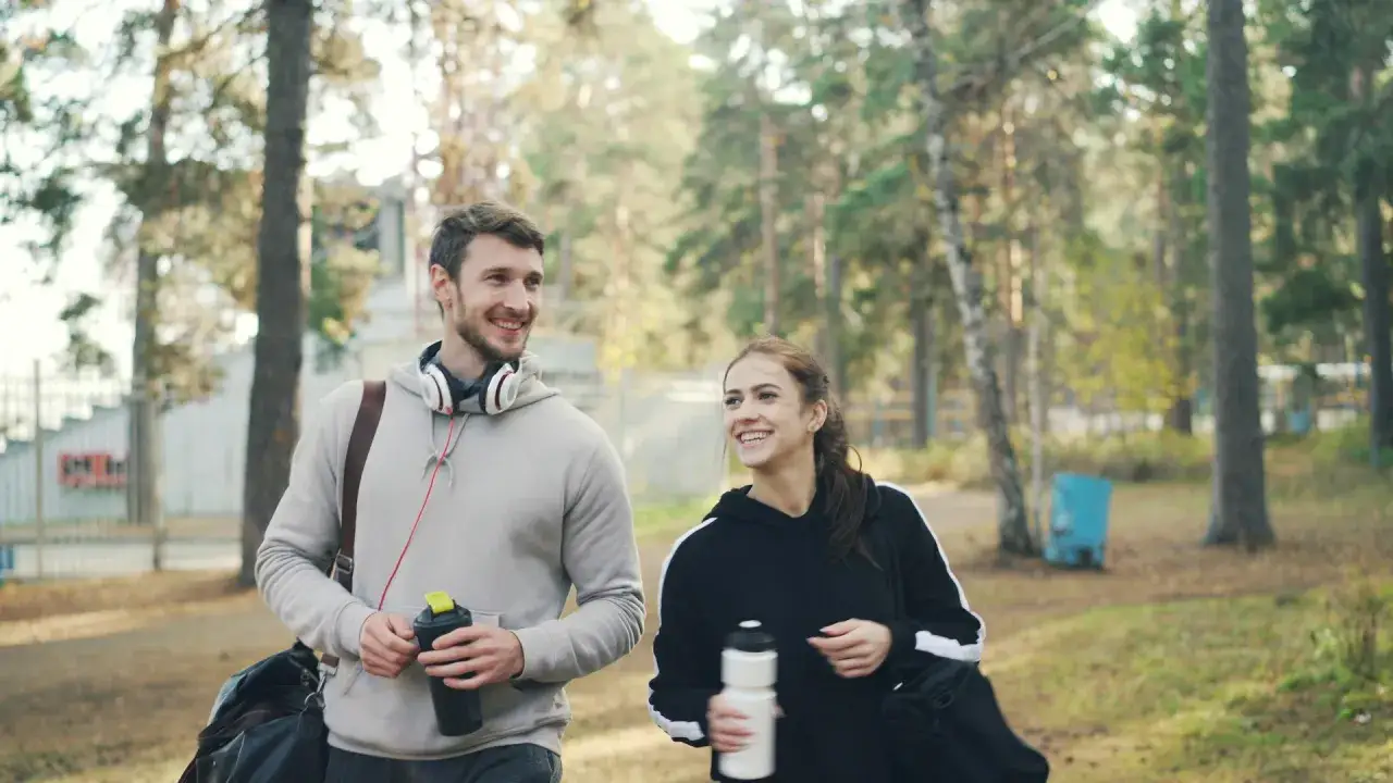 Gl&uuml;ckliches Paar im Wald, bereit f&uuml;r aerobe Ausdauer. Sie tragen Sporttaschen und Wasserflaschen.