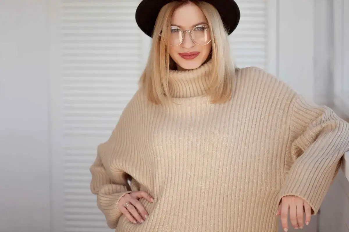 Kobieta w beżowym swetrze oversize i okularach, prezentująca modne stylizacje.