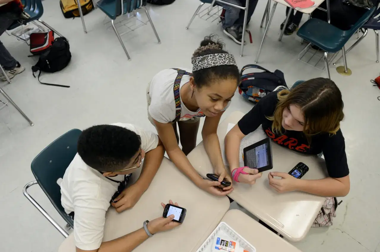 Schüler nutzen digitale Medien im Unterricht: Tablets und Smartphones werden für Lernzwecke eingesetzt, während sie an ihren Tischen sitzen und zusammenarbeiten.
