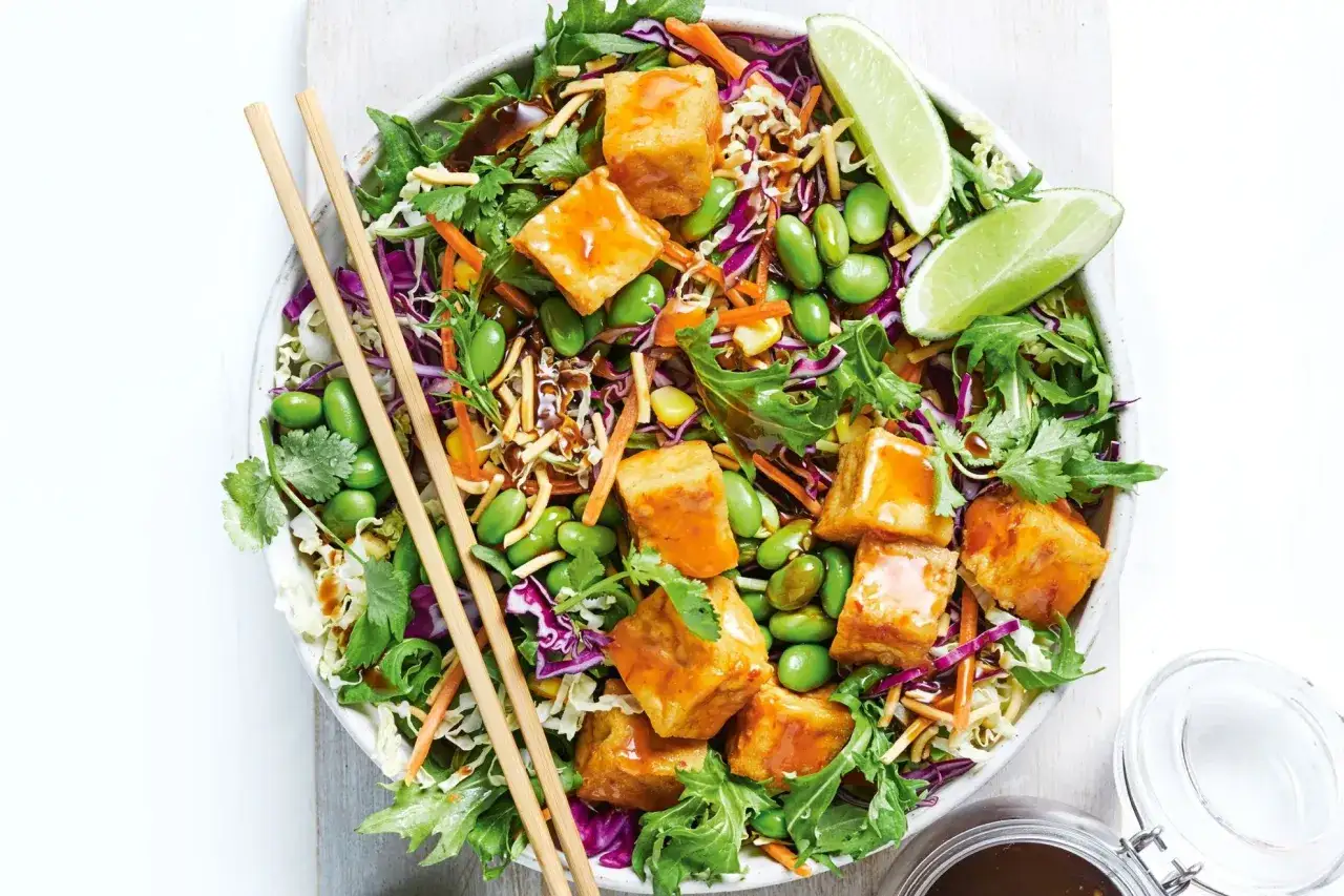 En matig sallad med krispiga grönsaker, edamamebönor, strimlad morot, rödkål och krispiga tofu-bitar, toppad med lime och en dressing.
