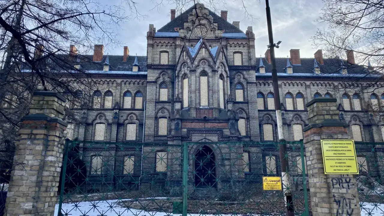 Mokrzeszów pałac, opuszczony, z zabitymi deskami oknami, otoczony zardzewiałym ogrodzeniem.