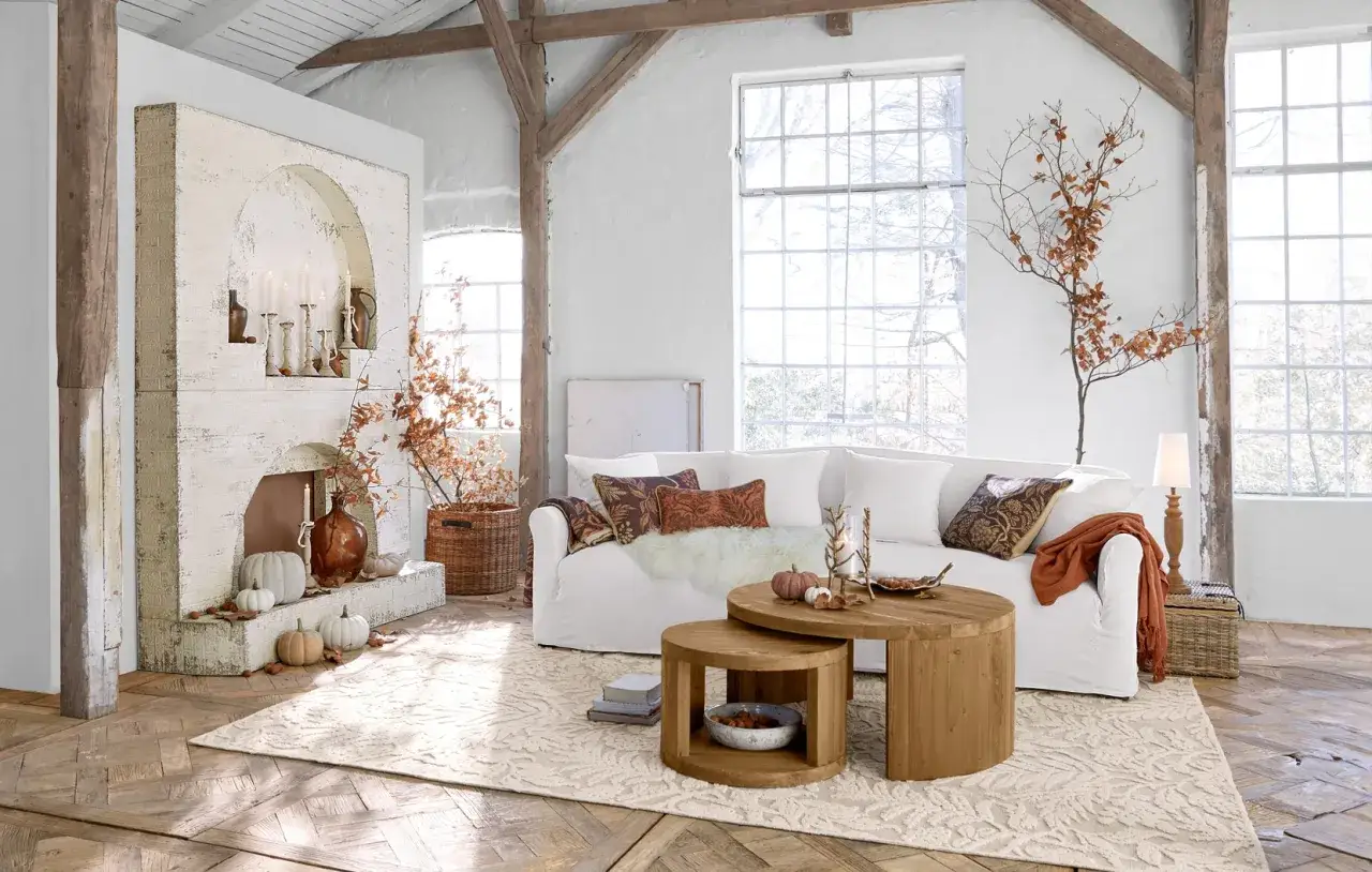 Gemütliches Wohnzimmer mit weißem Sofa, rustikalen Holztischen und Kamin. Tolle wanddeko ideen mit Zweigen und Kürbissen für eine herbstliche Atmosphäre.