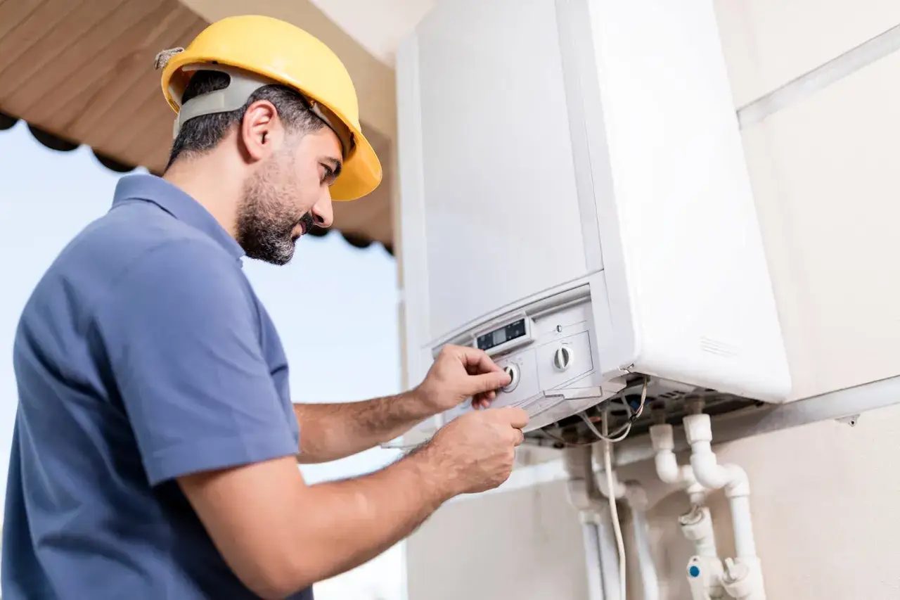 Technicien en casque jaune ajuste un bouton sur une chaudière. La durée d'entretien chaudière est optimisée pour votre confort.