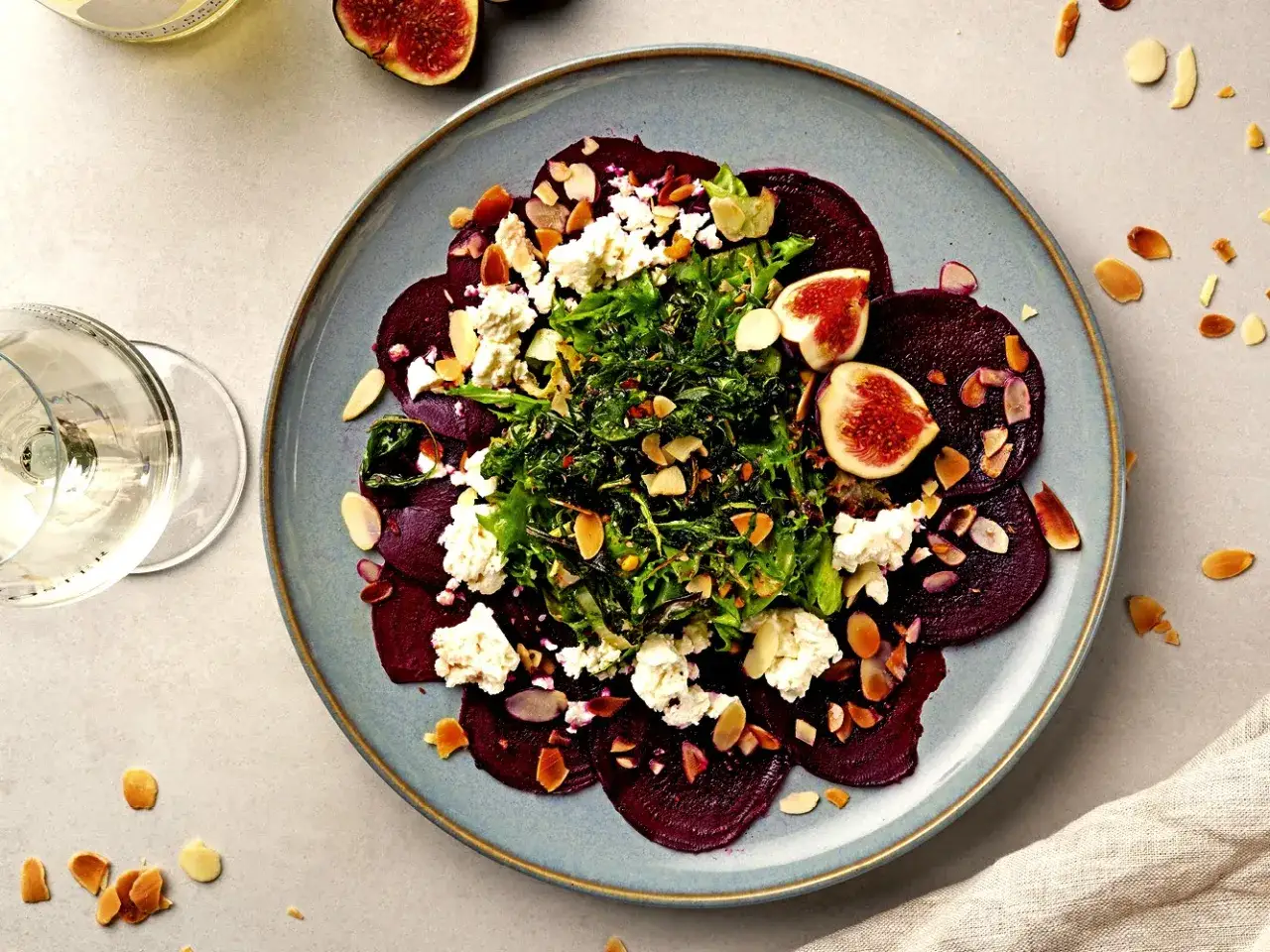 Rote Bete Carpaccio mit Ziegenkäse, Feigen und Mandelsplittern auf einem blauen Teller.