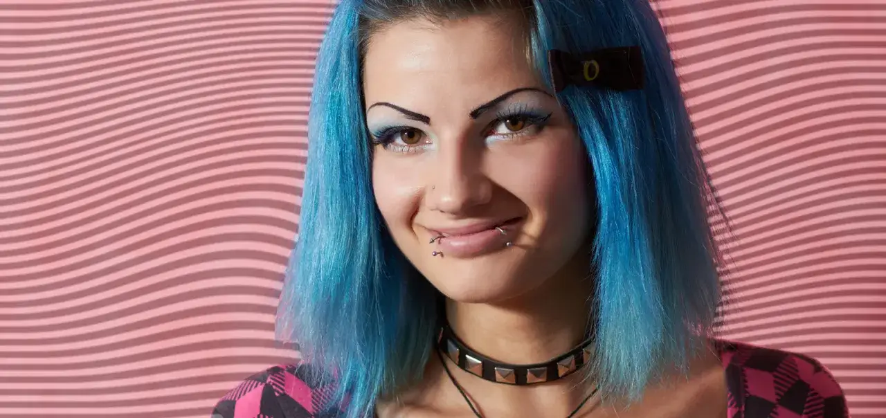 Uśmiechnięta dziewczyna z niebieskimi włosami i snake bite piercingiem na ustach.