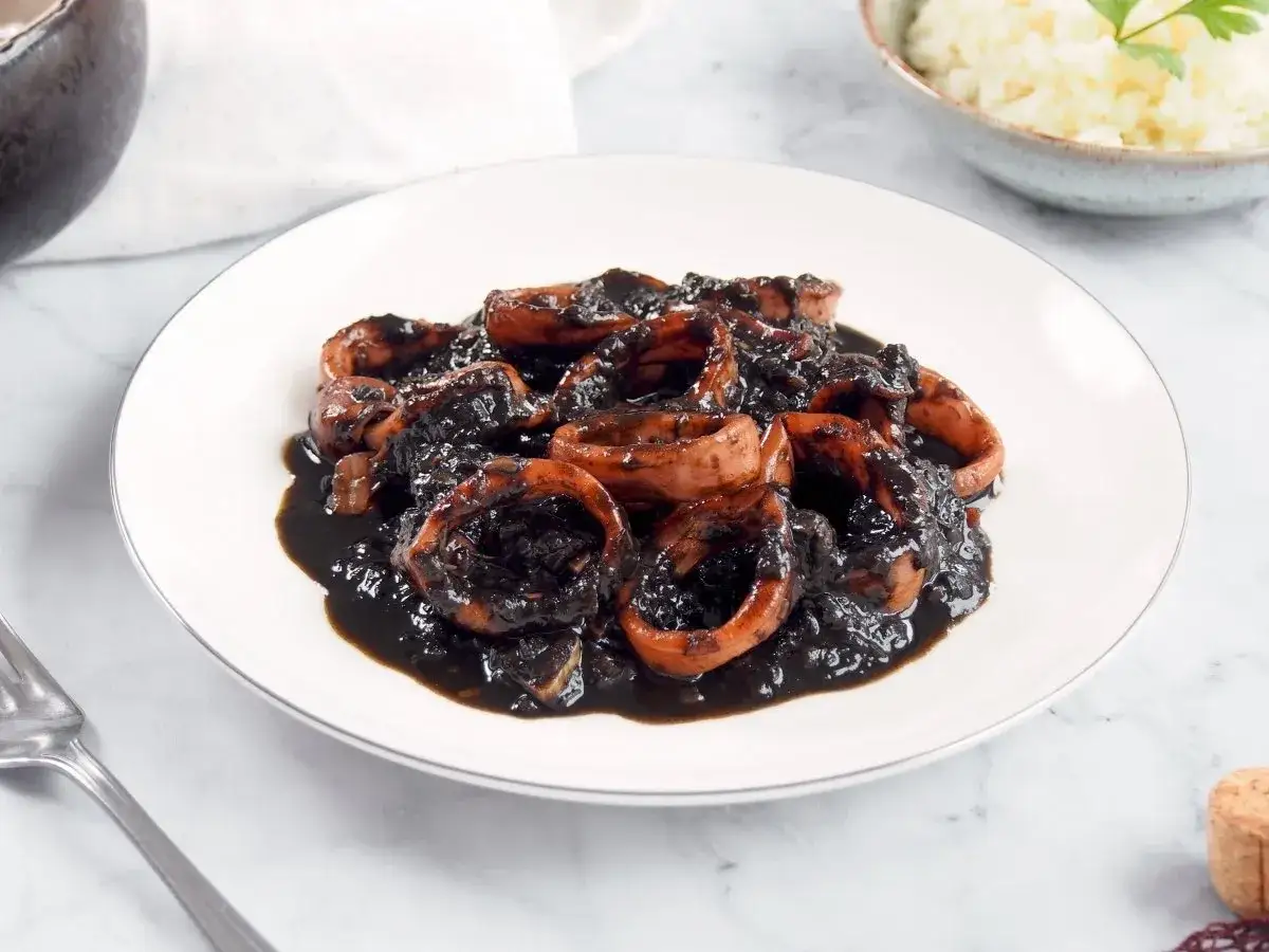 Calamares en su tinta, un plato tradicional espa&ntilde;ol con anillas de calamar cocinadas en su propia tinta, servido en un plato blanco.
