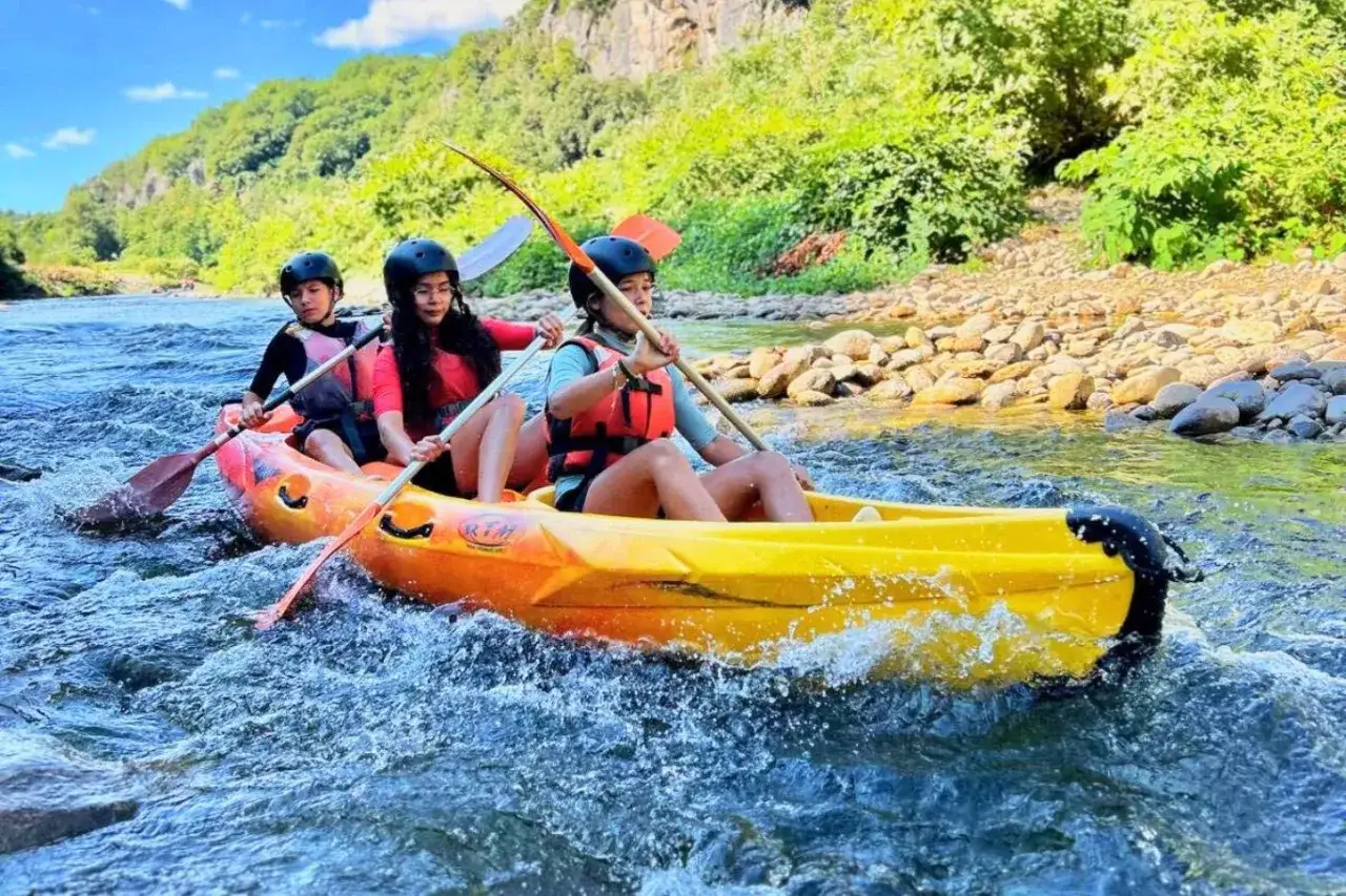 Trois jeunes profitent d'une activité canoe kayak sur une rivière aux eaux vives, entourés par une nature luxuriante.