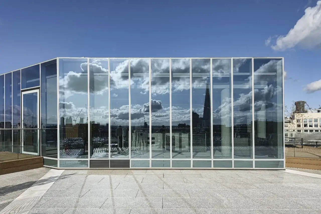 Moderne facciate architettoniche in vetro riflettono un cielo nuvoloso e lo skyline di una citt&agrave;, creando un gioco di luci e forme.