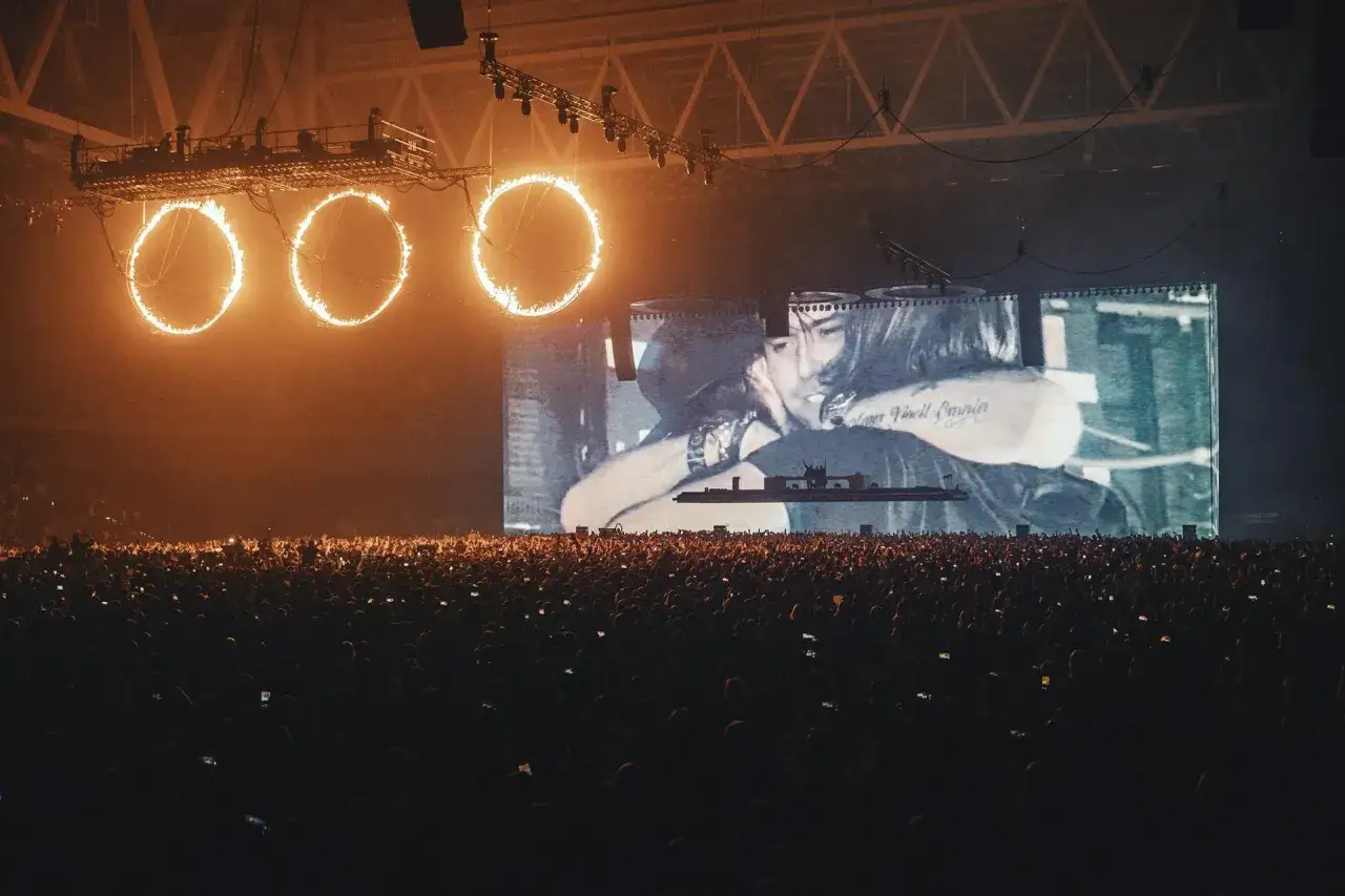 Koncert Swedish House Mafia w Polsce. Tłum ludzi, płonące obręcze nad sceną i wielki ekran z wizualizacjami.