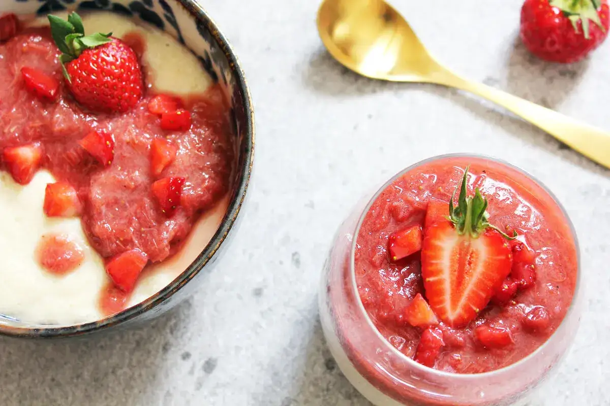 Veganes Grießbrei mit Erdbeerpüree und frischen Erdbeeren, serviert in einer Schale und einem Glas.