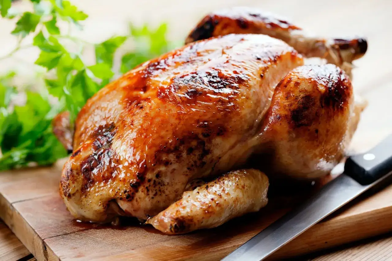 Un délicieux poulet rôti doré sur une planche en bois, prêt à être découpé. Quel vin avec un poulet rôti ? Un blanc fruité ou un rouge léger serait parfait.
