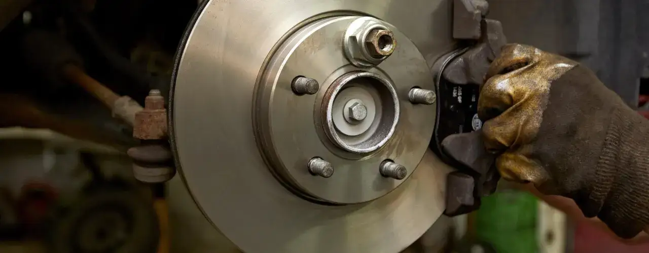 Mechaniker mit Handschuh montiert neue Bremsbeläge an einer Bremsscheibe. Informieren Sie sich, was kosten bremsen wechseln.