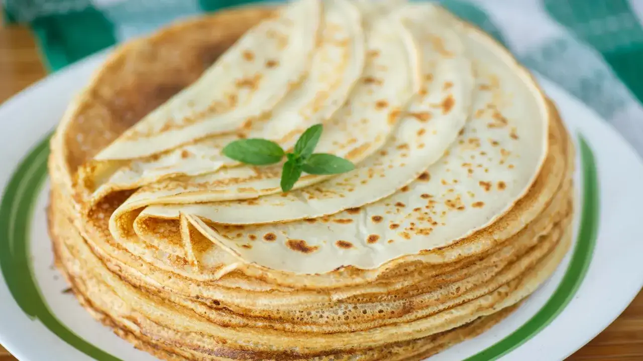 Ein Stapel goldbrauner Pfannkuchen, wie nach Omas Pfannkuchen Rezept, mit einem Minzblatt garniert.