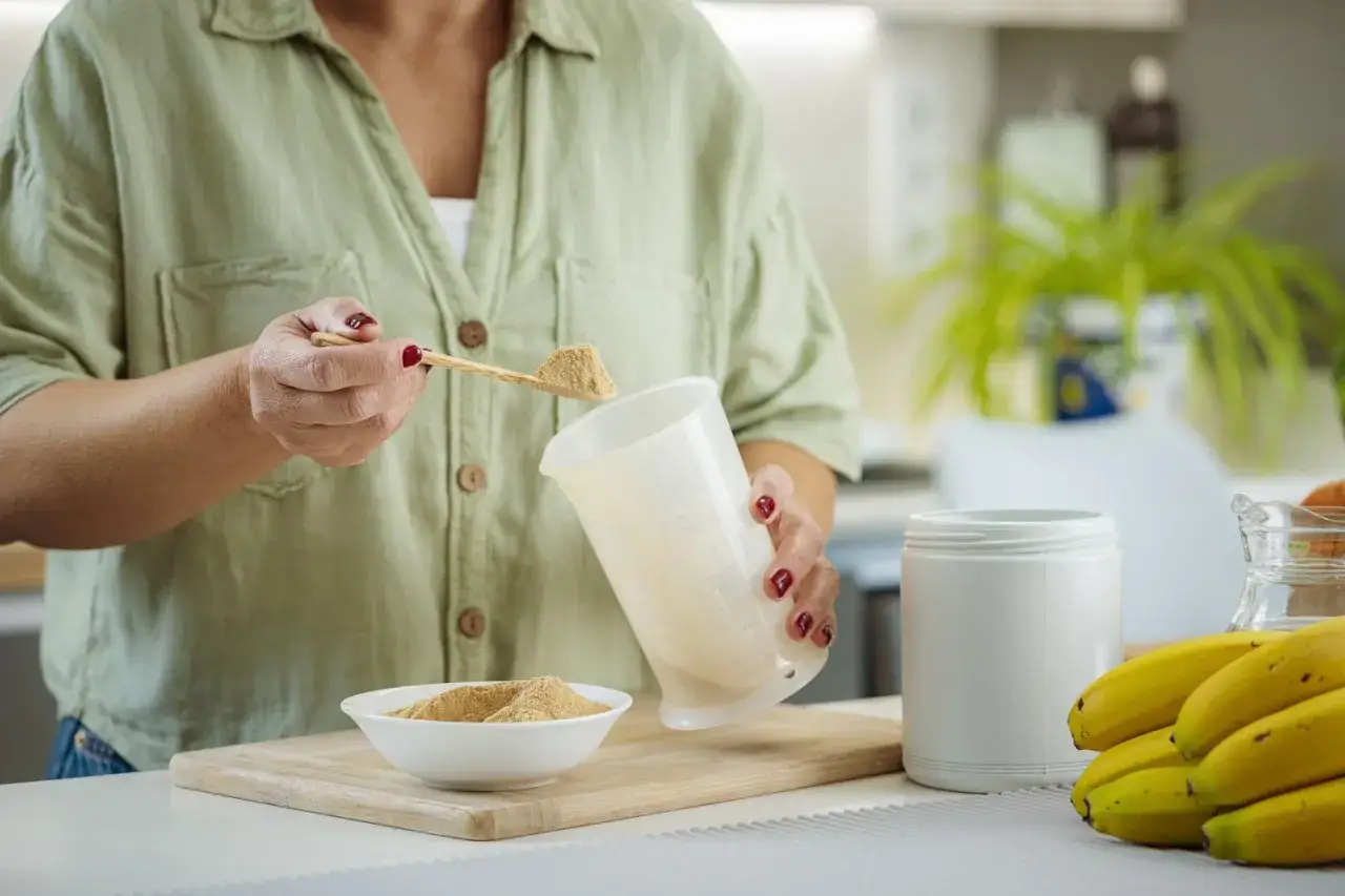 Frau bereitet einen protein shake abnehmen zu, indem sie Pulver aus einem L&ouml;ffel in einen Messbecher gibt.