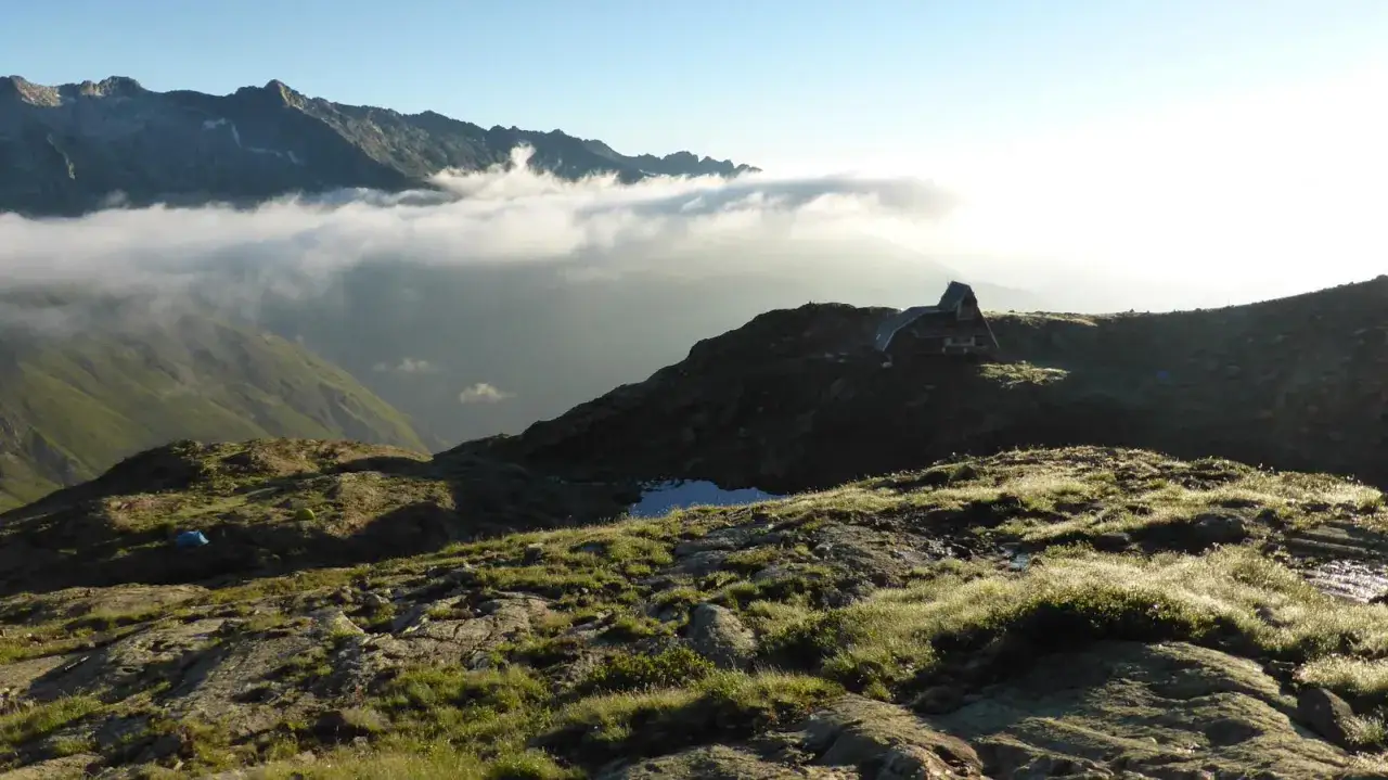 Refugio en la **Vall Ferrera** al amanecer, con niebla baja entre montañas y tiendas de campaña en la ladera.