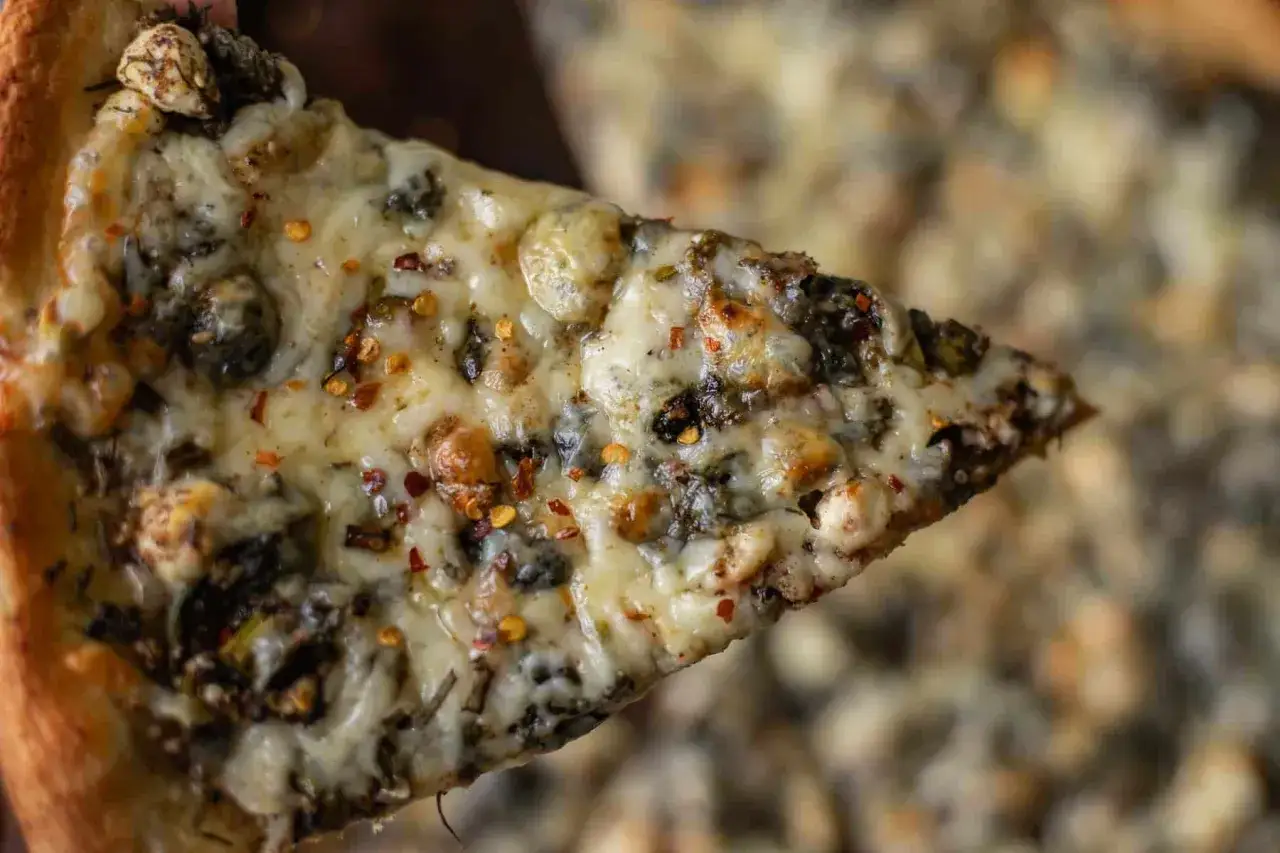 Kawałek pysznej pizzy ze szpinakiem, obficie posypanej serem i płatkami chili.