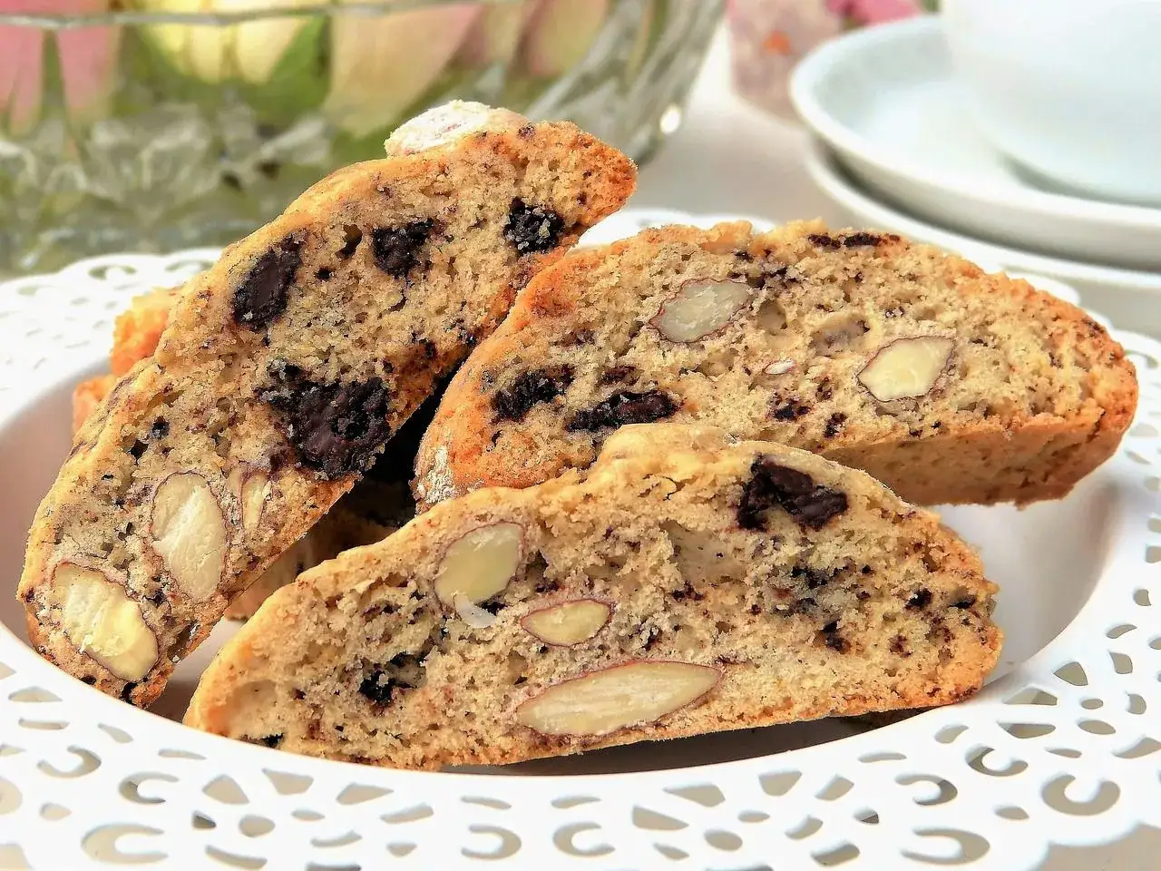 Biscotti con mandorle e gocce di cioccolato, dolci tipici toscani, serviti su un piatto bianco traforato.