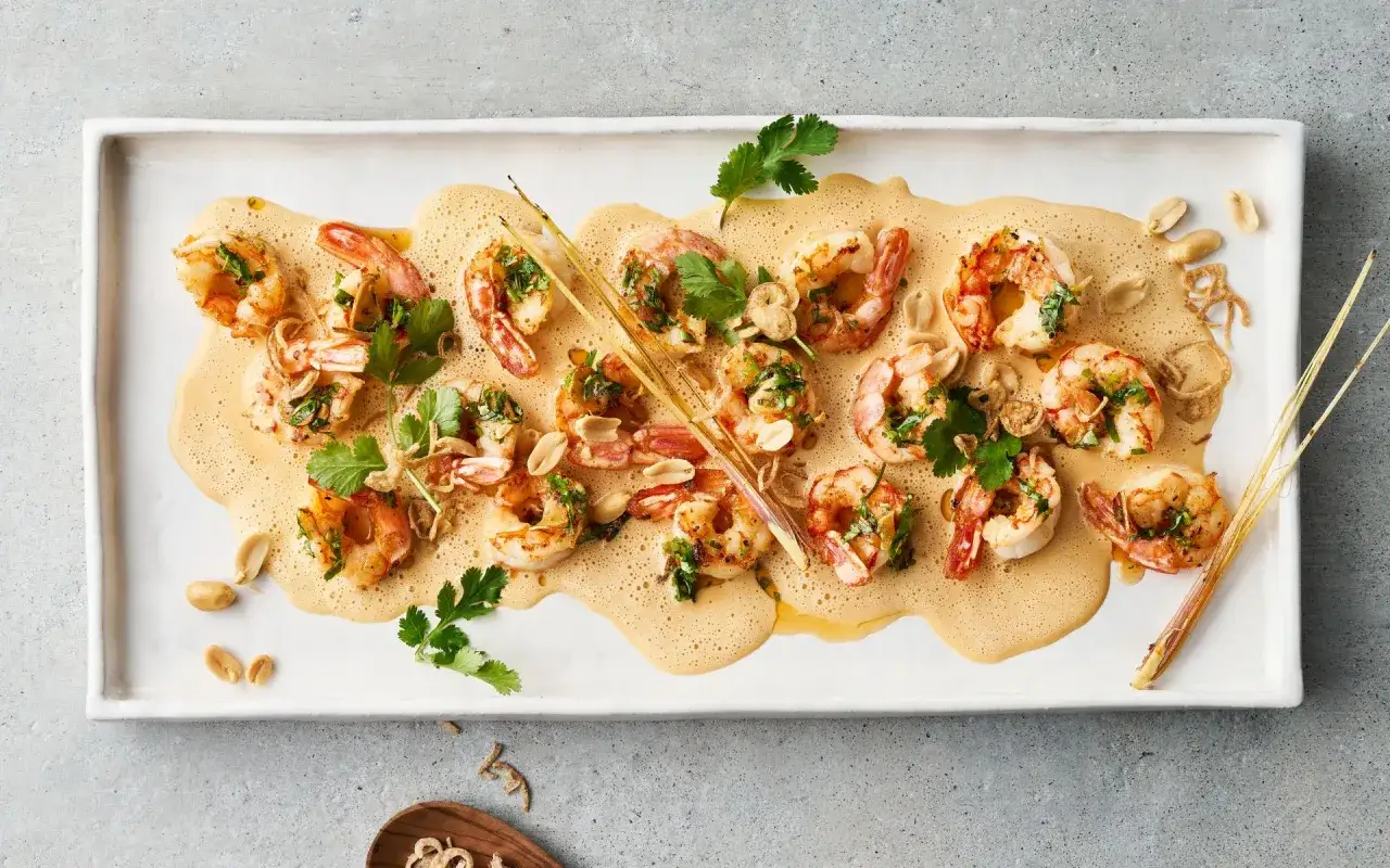 Gegrillte Garnelenarten zum Essen, serviert auf einer cremigen Sauce mit Koriander und Erdn&uuml;ssen.