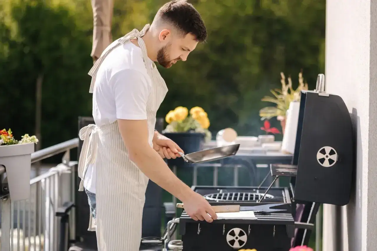 Mężczyzna w fartuchu przygotowuje się do grillowania na balkonie. Czy można robić grilla na balkonie? Tak, jeśli jest to bezpieczne i zgodne z przepisami.