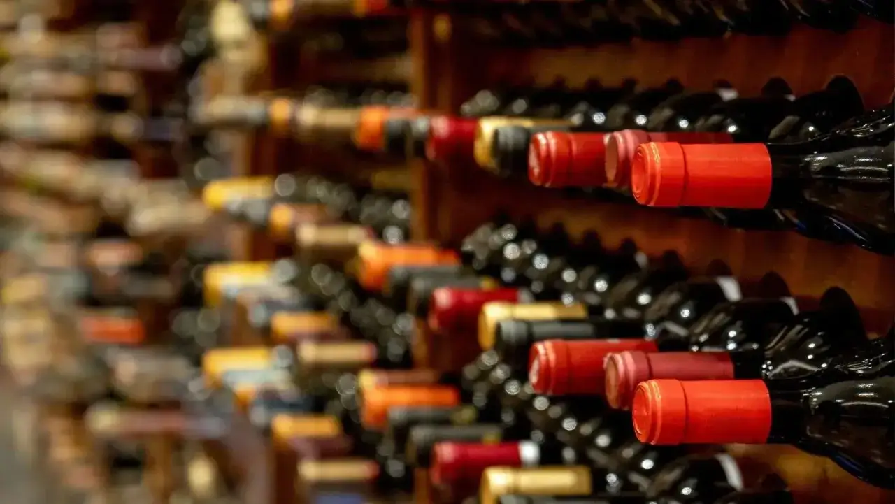 Scaffali pieni di bottiglie di vino, alcune con tappi rossi. Chiss&agrave; se il vino scade, ma l'attesa per l'assaggio &egrave; lunga.