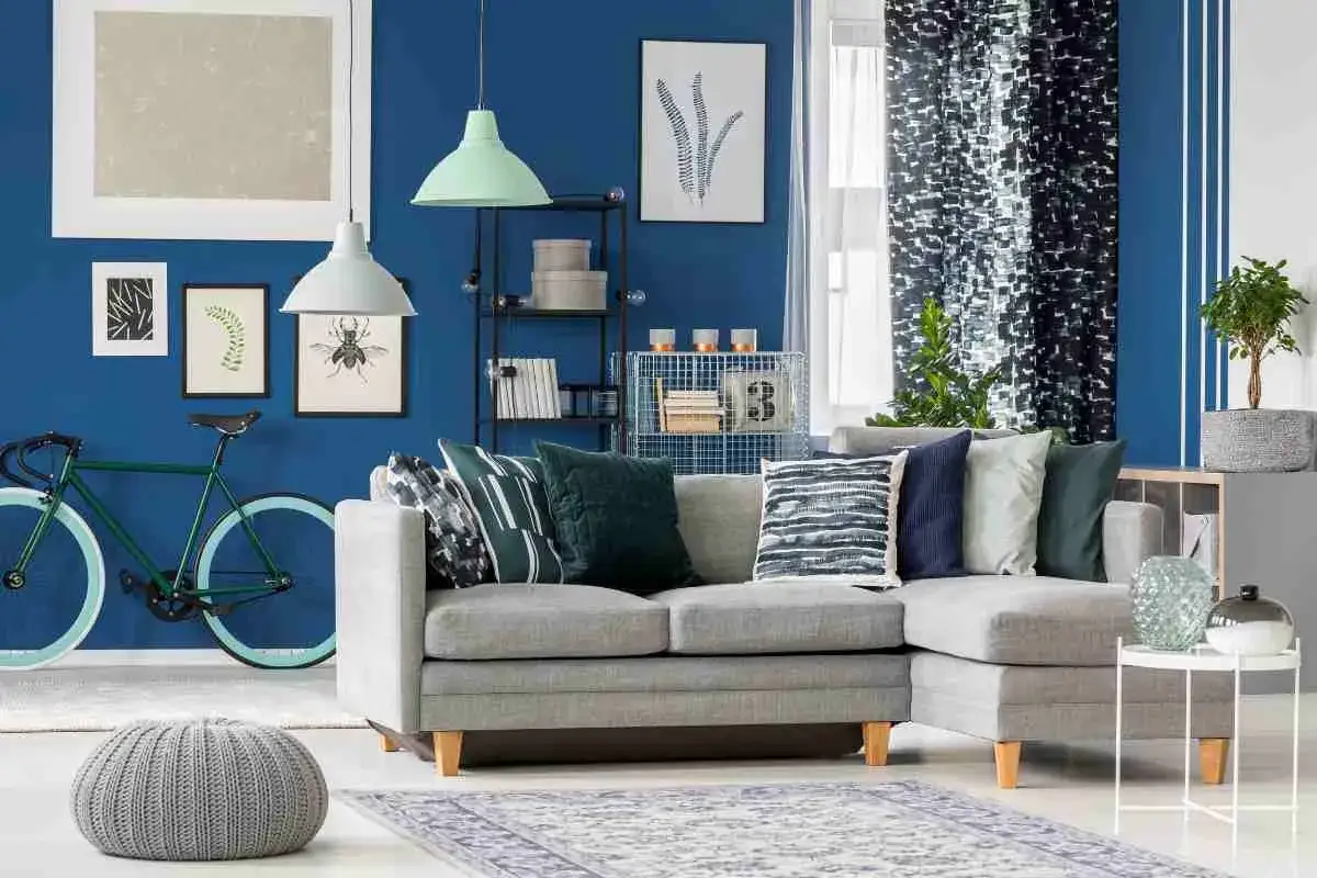 Un soggiorno moderno con divano grigio, cuscini a fantasia e una bicicletta verde. La parete blu intenso crea un'atmosfera con **colori freddi**.