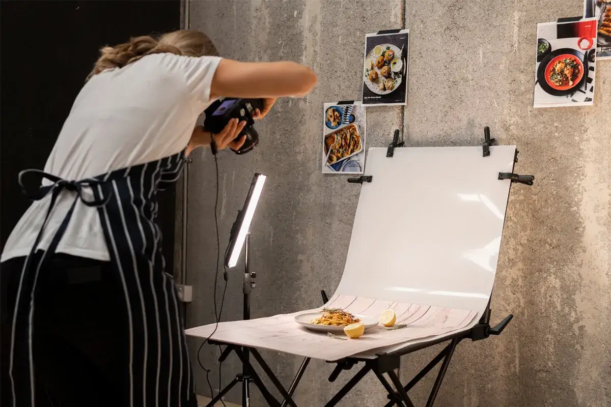 A photographer captures a delicious pasta dish for a tabletop photography project, using a light panel and backdrop.
