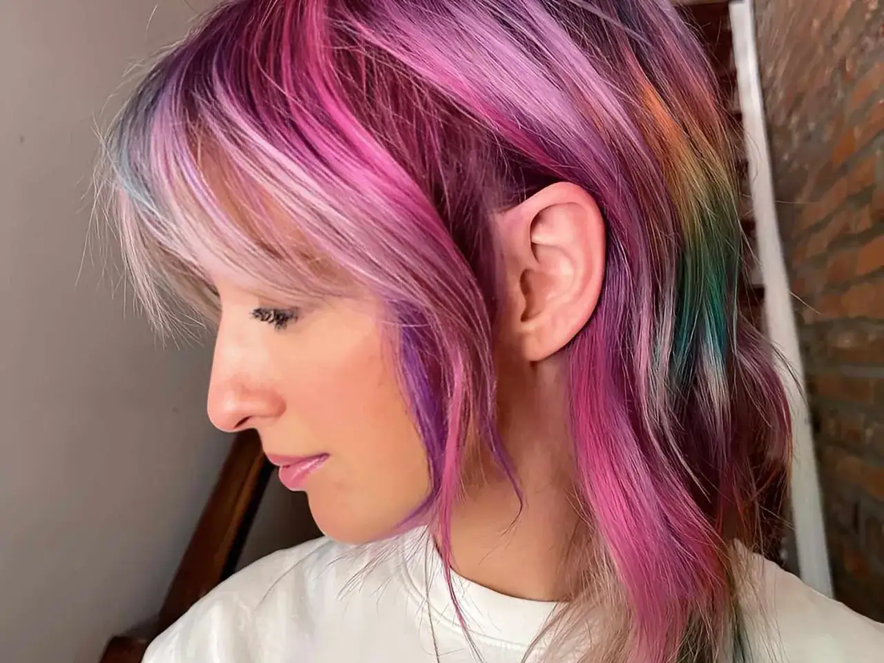 Ein Profilbild einer Frau mit auff&auml;lligen, bunten Haaren in Pink-, Lila-, Blau- und Gr&uuml;nt&ouml;nen.