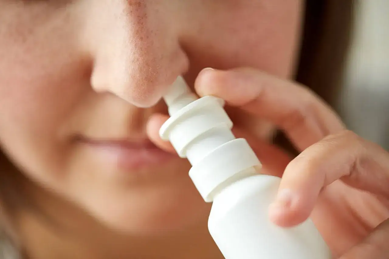 Kobieta aplikuje spray do nosa, szukając domowych sposobów na zatoki.