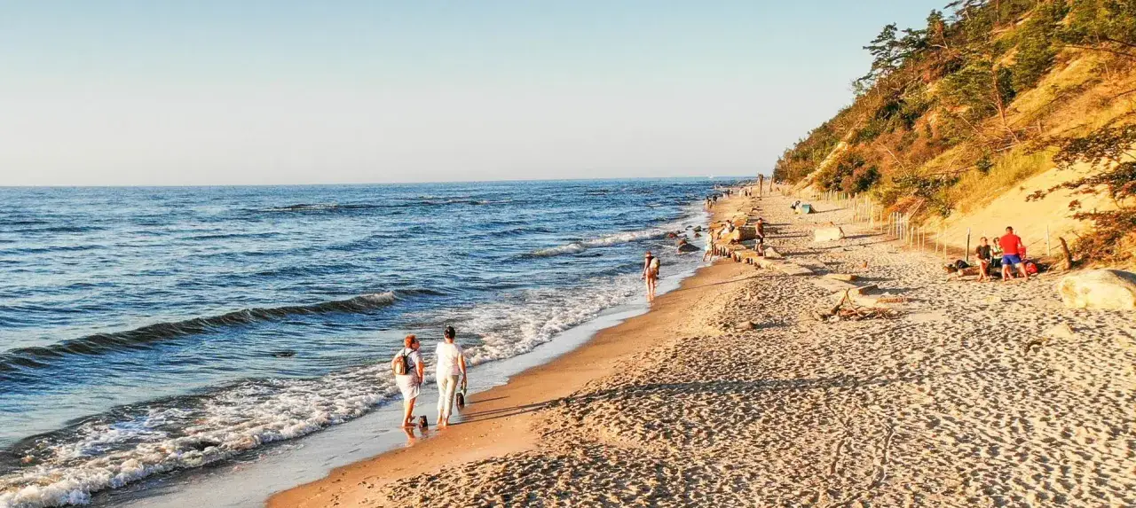 Piękna pogoda na czerwiec nad morzem. Ludzie spacerują po plaży, ciesząc się słońcem i łagodnymi falami.