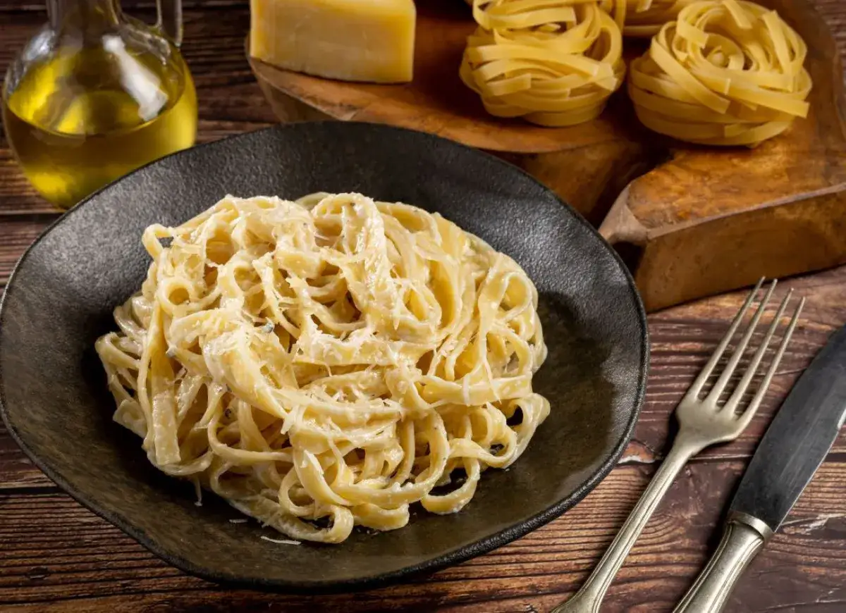 Pyszne fettuccine alfredo na talerzu, obok ser i oliwa. To klasyczne włoskie danie, które warto znać!