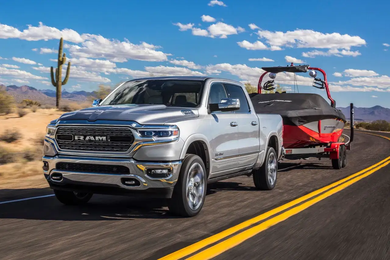 Srebrny pickup RAM 1500 z przyczepą i łodzią jedzie po pustynnej drodze.