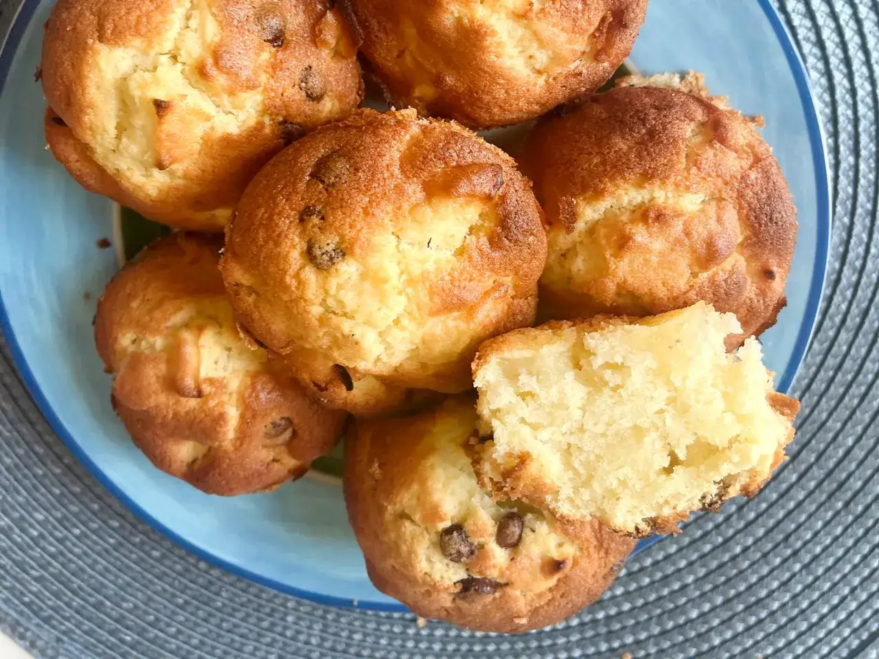 Saftige Apfelmus Muffins mit Schokost&uuml;ckchen auf einem blauen Teller. Einer ist aufgeschnitten und zeigt die lockere Textur.