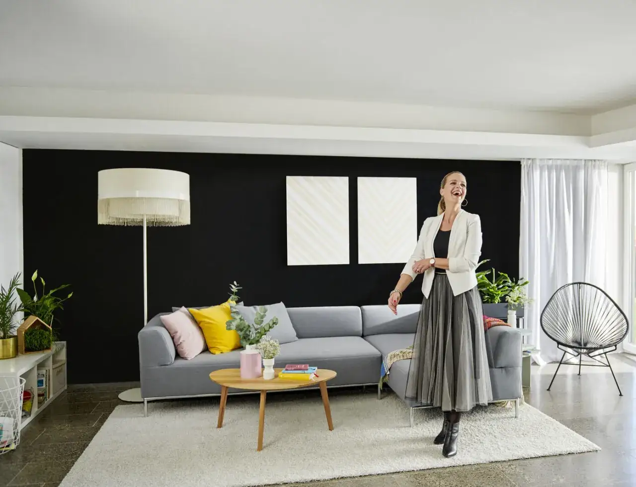 Frau lacht in modernem Wohnzimmer mit schwarzer Wand, bereit, die Wohnung zu streichen.
