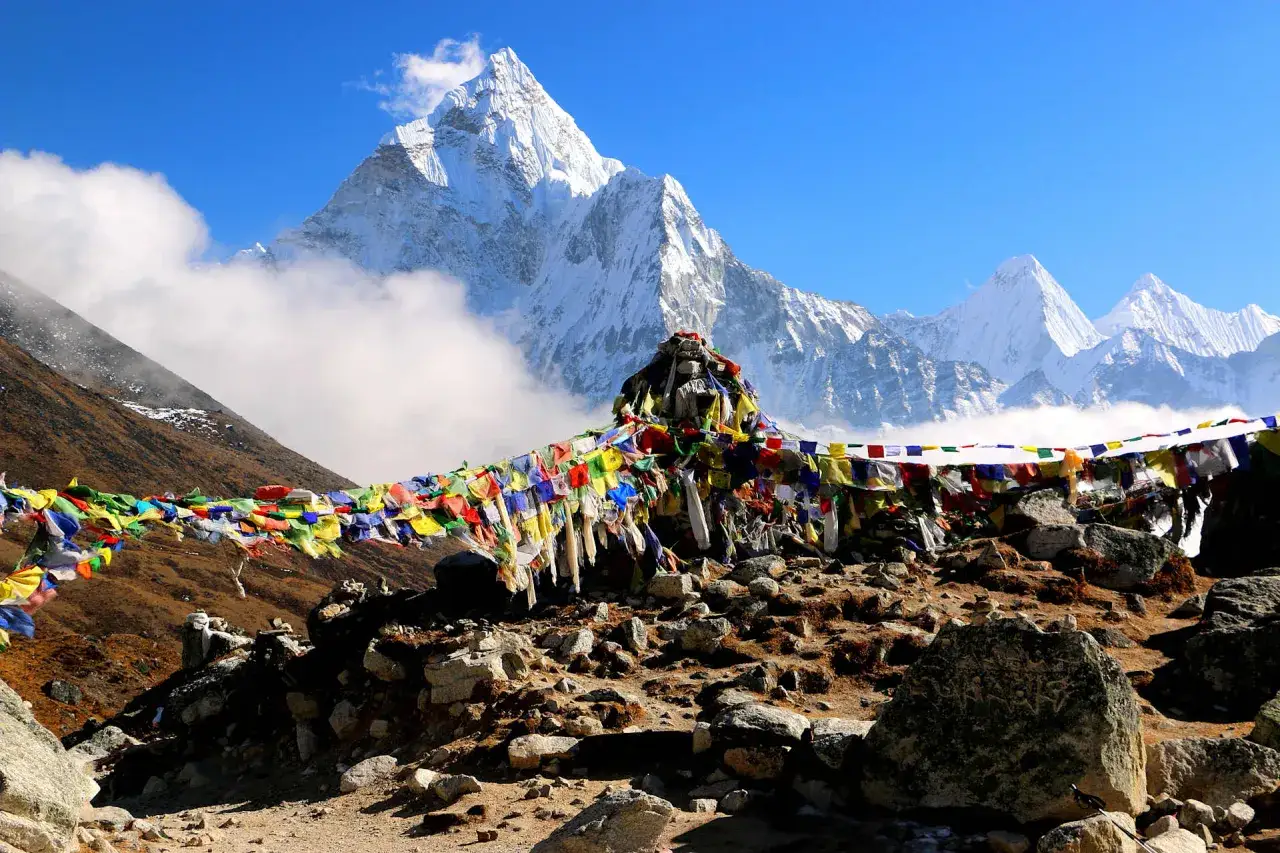Bunte Gebetsfahnen wehen im Wind vor majestätischen schneebedeckten Gipfeln. Ein unvergessliches Erlebnis beim Himalaya wandern.