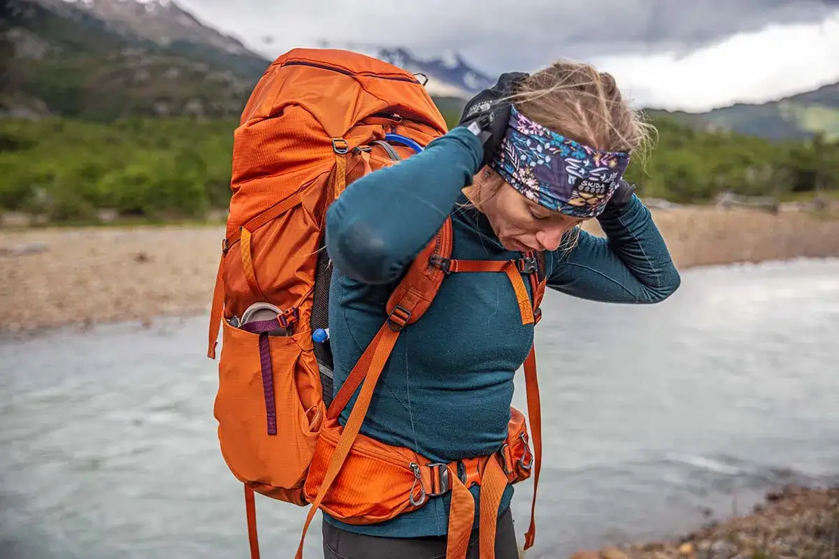 Randonneuse ajustant son bandeau, portant un grand sac &agrave; dos orange. La laine m&eacute;rinos, c'est quoi ? Une fibre naturelle id&eacute;ale pour le confort en montagne.