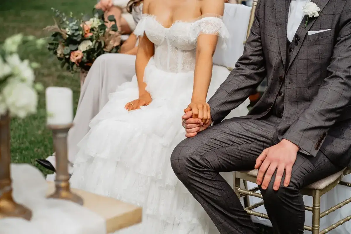 Para spowiedzi przedślubnej lub formalności w USC: panna młoda w koronkowej sukni i pan młody w garniturze trzymają się za ręce.