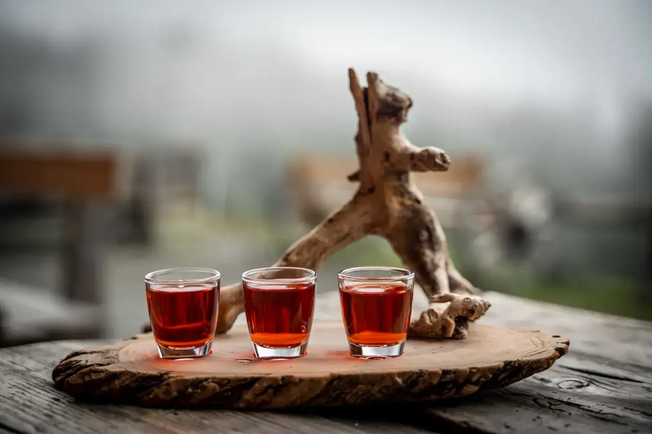 Drei Gläser mit bernsteinfarbenem Schnaps zum selber machen, auf einem Holzbrett mit einer bizarren Wurzel.