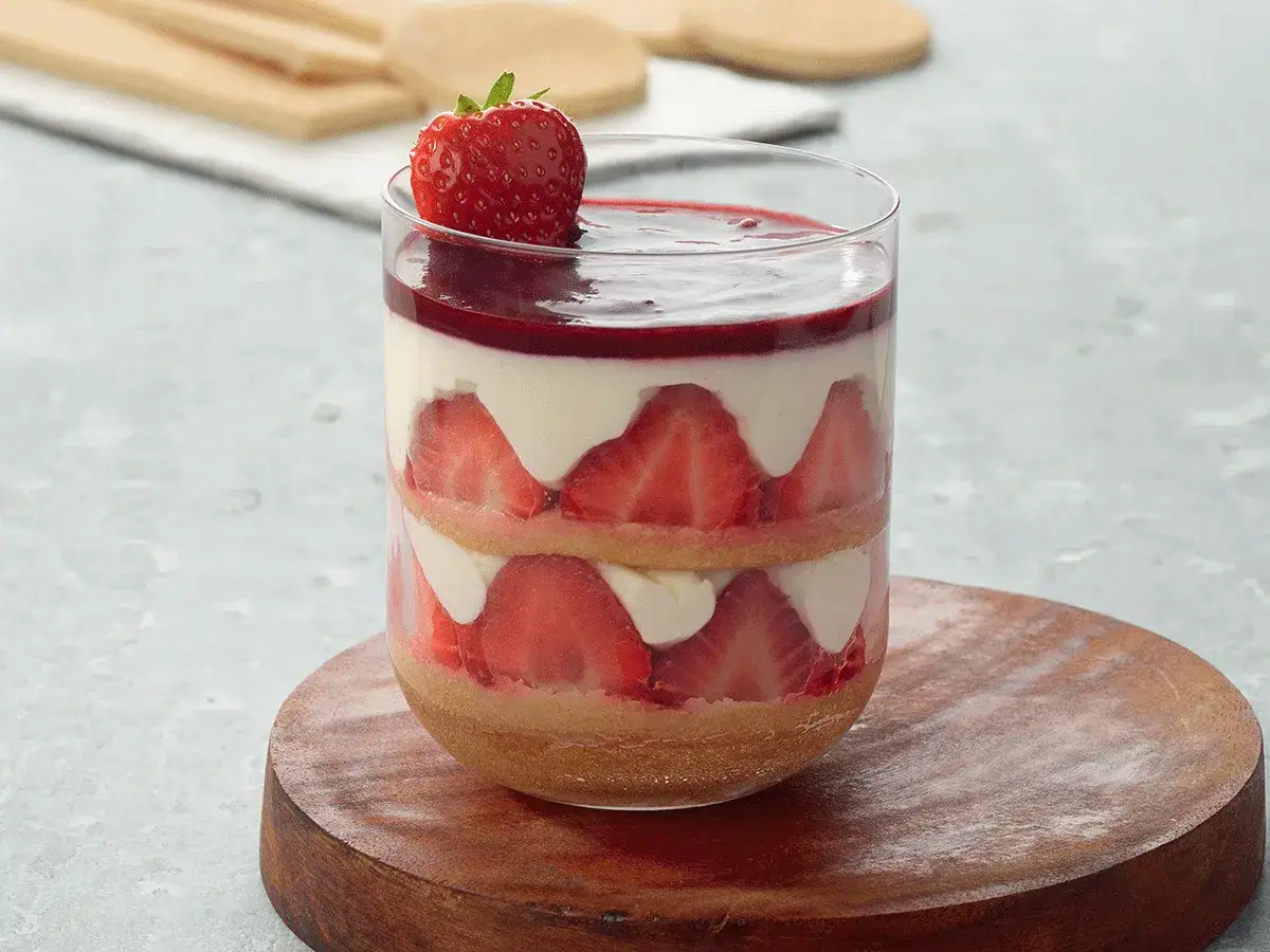 Un délicieux tiramisu fraise en verrine, superposant biscuits, crème et fruits rouges, couronné d'une fraise fraîche.
