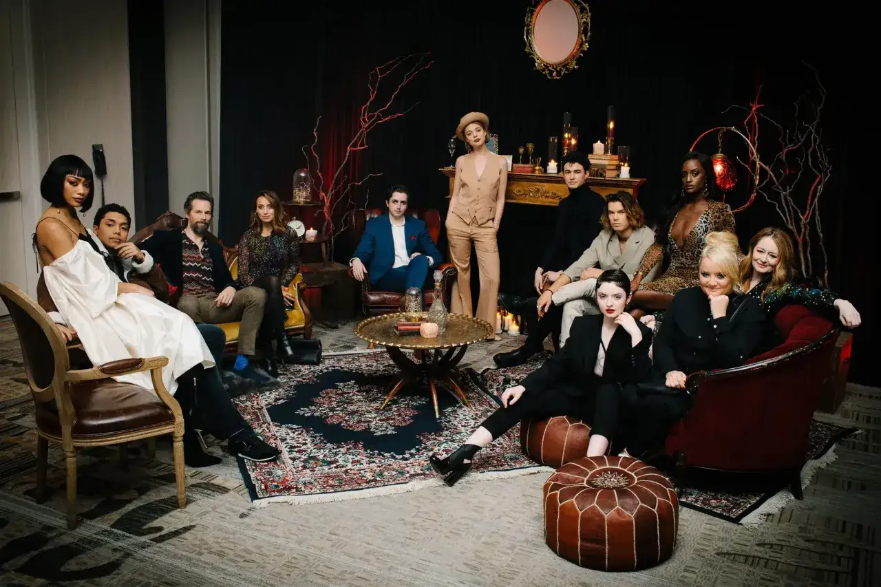 Chilling adventures of Sabrina obsada w mrocznym, stylowym otoczeniu. Aktorzy siedzą i stoją, tworząc grupowe zdjęcie.