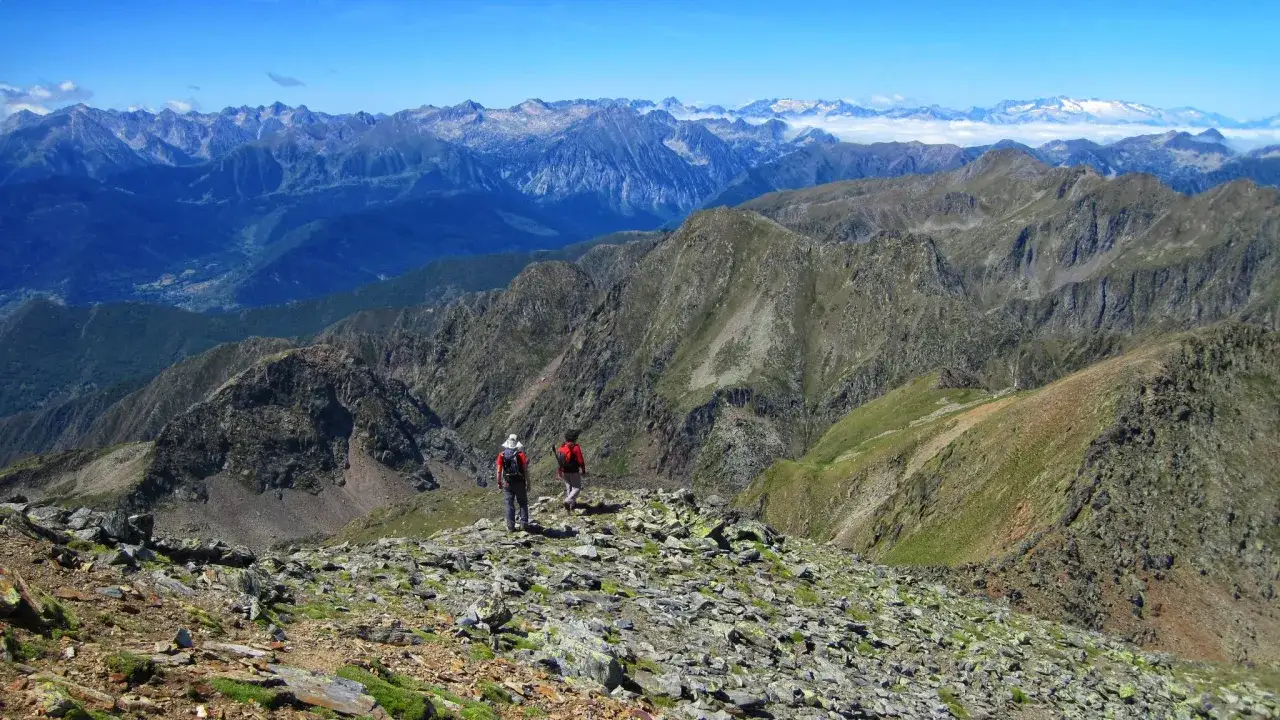 Dos excursionistas exploran las impresionantes **rutas de Esterri d'Àneu**, con picos nevados al fondo.